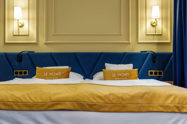 Pokój Lux w hotelu Le Mont: łóżko z musztardową narzutą i poduszkami z logo hotelu, granatowy tapicerowany zagłówek